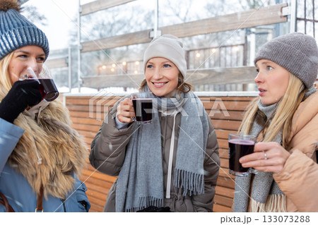 Portrait three pretty young adult woman friends enjoy laughing drinking hot mulled wine at Christmas market outdoors cold winter day. People having fun celebrate new year time street cafe outside Portrait three pretty young adult woman friends enjoy laughing drinking hot mulled wine at Christmas market outdoors cold winter day. People having fun celebrate new year time street cafe outside 133073288