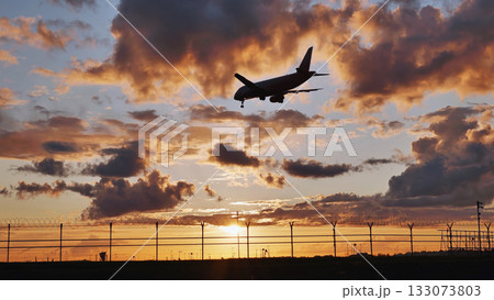 Passenger airplane landing at sunset over airport fence 133073803