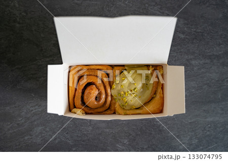 Classic and pistachio cinnamon rolls arranged in a takeout cardboard box, viewed from above. Concept of bakery, pastry, takeaway, breakfast, indulgence. Classic and pistachio cinnamon rolls arranged in a takeout cardboard box, viewed from above. Concept of bakery, pastry, takeaway, breakfast, indulgence. 133074795