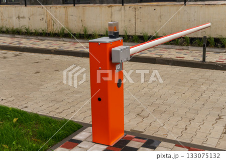 Bright orange crossbar barrier stands by a paved parking lot, designed to manage vehicle entry and exit efficiently 133075132