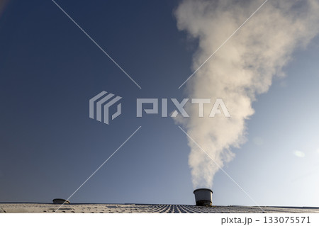 smoke coming from a wide pipe against a blue sky background, white steam coming from a pipe during heating of a large industrial premises in cold weather 133075571