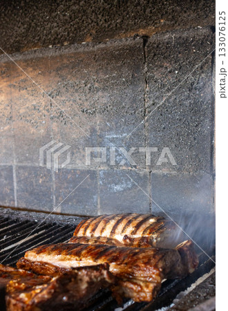 Pork ribs grilling over hot coals on an authentic argentine barbecue, showing flavorful meat cooking with rising smoke, perfect for a traditional outdoor meal Pork ribs grilling over hot coals on an authentic argentine barbecue, showing flavorful meat cooking with rising smoke, perfect for a traditional outdoor meal 133076125
