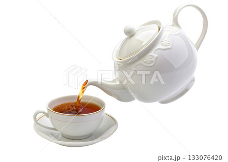 Hot tea pouring from classic white teapot into matching porcelain teacup, creating dynamic stream of aromatic beverage for cozy relaxing moment 133076420