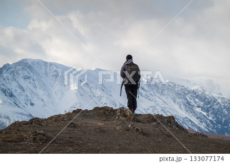 Hiker standing on rocky edge overlooking snow covered mountains in remote wilderness Hiker standing on rocky edge overlooking snow covered mountains in remote wilderness 133077174