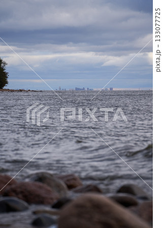 Distant city skyline over Gulf of Finland with stones and waves in foreground. 133077725