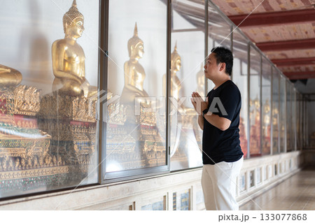 A man pays respect to the golden Buddha statues inside a temple, representing the cultural beauty of faith and traditional Thai spirituality. 133077868