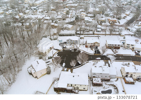 Snow blankets residential neighborhood in winter, quiet streets houses surrounded by trees Snow blankets residential neighborhood in winter, quiet streets houses surrounded by trees 133078721