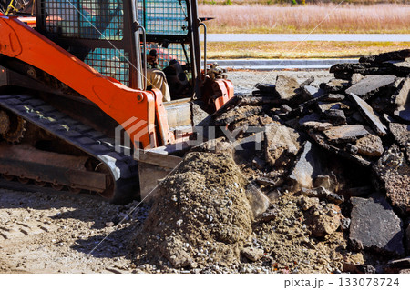 Construction equipment working on site with piles of broken asphalt debris 133078724