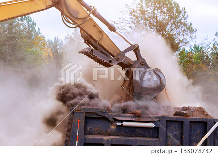 Heavy machinery digs dumps earth at construction site in dusty conditions Heavy machinery digs dumps earth at construction site in dusty conditions 133078732