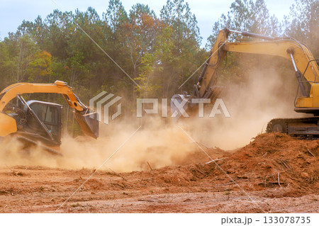 Excavators working on land clearing project in autumn landscape with dust clouds rising Excavators working on land clearing project in autumn landscape with dust clouds rising 133078735