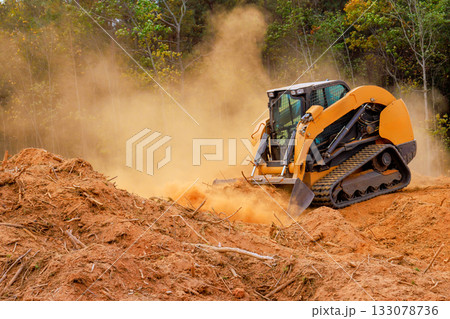 Heavy machinery clears land in forested area with visible dust dirt clouds 133078736