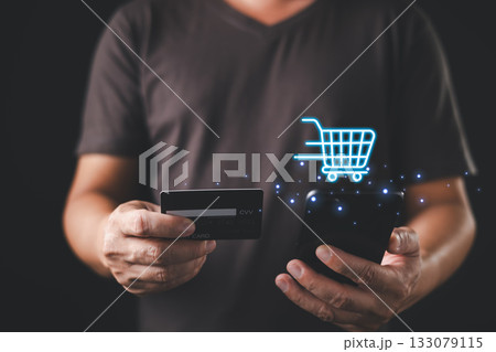 A person holds a credit card and smartphone while a glowing digital shopping cart icon floats above, symbolizing mobile commerce, online shopping, and secure digital payment transactions. A person holds a credit card and smartphone while a glowing digital shopping cart icon floats above, symbolizing mobile commerce, online shopping, and secure digital payment transactions. 133079115