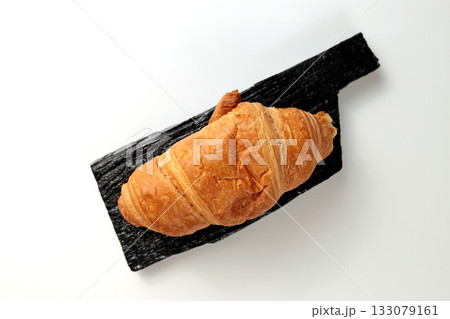 Crispy hot croissant on a black rectangular wooden board on a white background 133079161