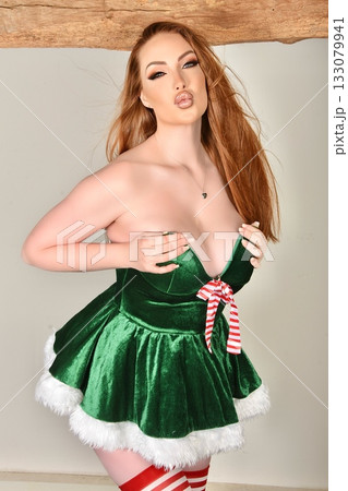 Beautiful, tall, shapely redhead model dressed as a Sexy Santa and Elf, posing against a wall in an old house 133079941