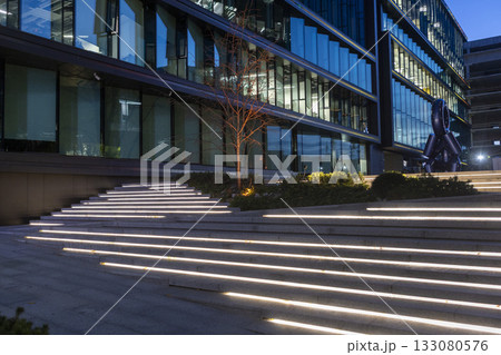 An evening view of a business center with modern glass and steel architecture and a square with a flowerbed next to it. An evening view of a business center with modern glass and steel architecture and a square with a flowerbed next to it. 133080576