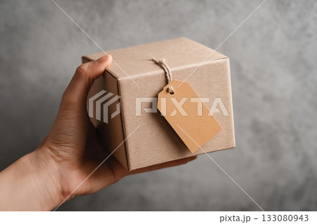 Person Holding a Cardboard Box With a Blank Tag in a Minimalist Setting Generative AI 133080943