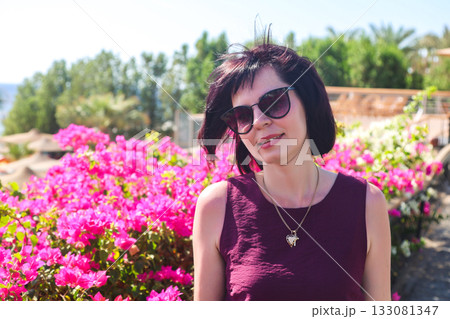 A slender woman in a dress near a flower bed with the sea in the background 133081347