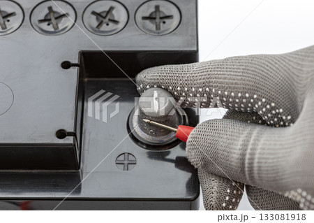 Gloved hand measures positive terminal of car battery with red probe for safety and precision 133081918
