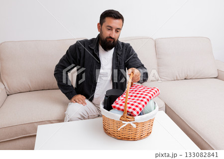 Caucasian male preparing picnic basket on living room sofa 133082841