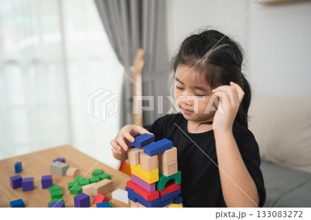 Young Child Engaged in Creative Play with Colorful Building Blocks in Cozy Indoor Space, Focused on Constructing Tower of Various Shapes 133083272