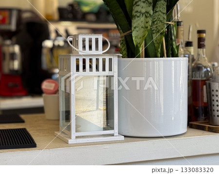 White decorative lantern beside potted plant on cafe counter. Scandinavian minimal style, modern interior simplicity, and natural atmosphere. 133083320