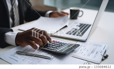 Close-up of hands calculating financial data using calculator and laptop. Business professional analyzing reports and invoices at modern office desk. Finance and accounting concept Close-up of hands calculating financial data using calculator and laptop. Business professional analyzing reports and invoices at modern office desk. Finance and accounting concept 133084612