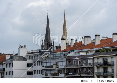 Bayonne cityscape with cathedral spires and residential buildings under a cloudy sky. Bayonne cityscape with cathedral spires and residential buildings under a cloudy sky. 133084685