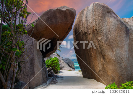 A narrow sandy path winds between granite boulders at Anse Source d'Argent, La Digue, Seychelles, framing turquoise waves and islands in warm late afternoon light. A narrow sandy path winds between granite boulders at Anse Source d'Argent, La Digue, Seychelles, framing turquoise waves and islands in warm late afternoon light. 133085011