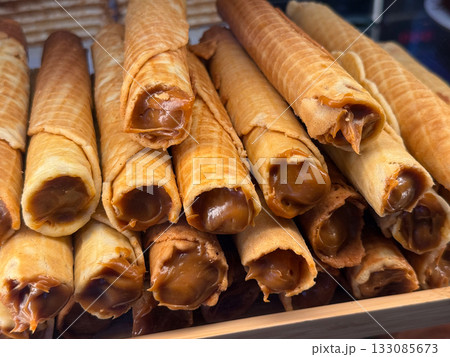 Waffle rolls filled with caramel cream on display close-up. Confectionery production, dessert craftsmanship and sweet pastry tradition. Waffle rolls filled with caramel cream on display close-up. Confectionery production, dessert craftsmanship and sweet pastry tradition. 133085673