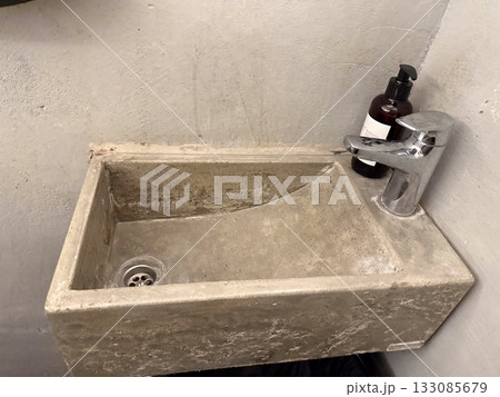 Minimal concrete sink with chrome faucet in small restroom. Industrial interior design, urban architecture, and functionality in everyday space. Minimal concrete sink with chrome faucet in small restroom. Industrial interior design, urban architecture, and functionality in everyday space. 133085679
