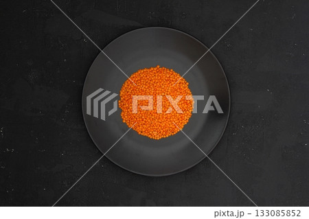 Red lentils in black plate on black stone table background. Top view, copy space. Flat lay. 133085852