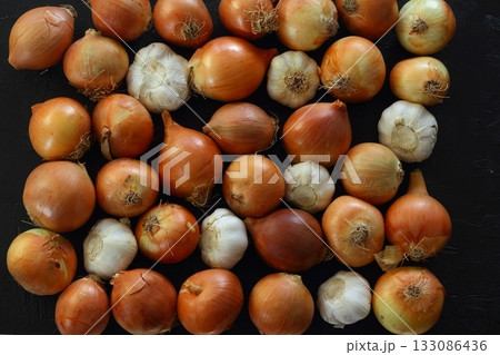 Onions and garlic over black background. Still-life of onions and falling garlic on black background 133086436