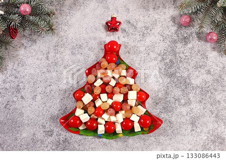 Traditional Christmas tree-shaped holiday salad with feta cheese, tomatoes, grapes, olives, and honey, topped with fir branches and decorations, dish decoration idea, Christmas and New Year's dishes 133086443