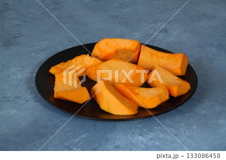 Slices of raw pumpkin with orange-yellow flesh in stainless steel bowl on a black background Slices of raw pumpkin with orange-yellow flesh in stainless steel bowl on a black background 133086458