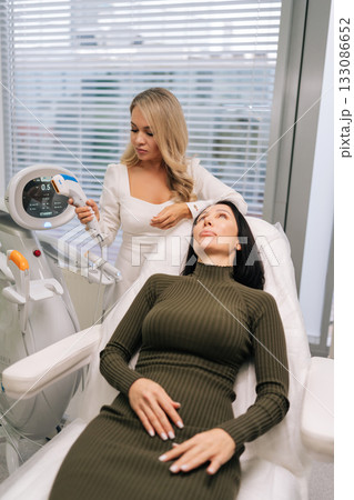 Vertical shot of woman receiving non-invasive ultrasound facial lifting and skin-tightening treatment in professional clinic, promoting anti-aging, collagen stimulation and youthful complexion. Vertical shot of woman receiving non-invasive ultrasound facial lifting and skin-tightening treatment in professional clinic, promoting anti-aging, collagen stimulation and youthful complexion. 133086652