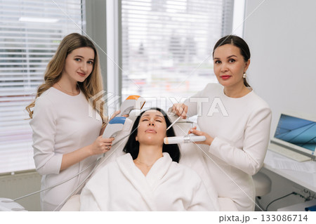 Female client receiving various professional aesthetic treatments including ultrasound and other advanced devices by cosmetologists for skin care and rejuvenation in beauty clinic. Female client receiving various professional aesthetic treatments including ultrasound and other advanced devices by cosmetologists for skin care and rejuvenation in beauty clinic. 133086714