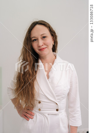 Woman medical professional in stylish white uniform stands confidently indoors against white background, conveying expertise and modern clinic or hospital professionalism. Concept of healthy lifestyle Woman medical professional in stylish white uniform stands confidently indoors against white background, conveying expertise and modern clinic or hospital professionalism. Concept of healthy lifestyle 133086718