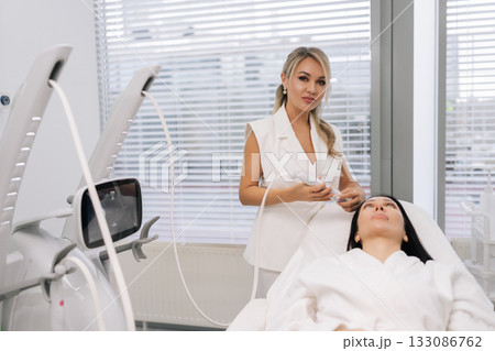Portrait of cosmetologist female performing microneedling anti-aging skincare treatment on woman face in modern beauty clinic, promoting rejuvenation and wellness. Concept of beauty, facial antiaging. 133086762