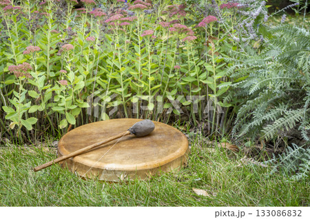 handmade, native American style, shaman frame drum covered by goat skin with a beater in a backyard handmade, native American style, shaman frame drum covered by goat skin with a beater in a backyard 133086832