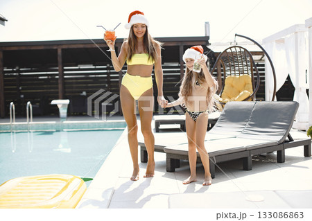 A funny woman with a child in Christmas hats by pool. Christmas celebration concept. Christmas day. Lifestyle. Pool background. A funny woman with a child in Christmas hats by pool. Christmas celebration concept. Christmas day. Lifestyle. Pool background. 133086863