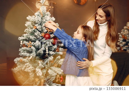 People reparing for Christmas. Mother playing with her daughter. Family is resting in a festive room. Child in a blue sweater. People reparing for Christmas. Mother playing with her daughter. Family is resting in a festive room. Child in a blue sweater. 133086911