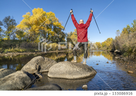 senior male hiker with trekking poles on a shore of the Poudre River in Fort Collins, Colorado, in a fall scenery senior male hiker with trekking poles on a shore of the Poudre River in Fort Collins, Colorado, in a fall scenery 133086916