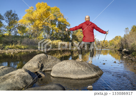 senior make hiker in his 70s with trekking poles on a shore of the Poudre River in Fort Collins, Colorado, fall scenery 133086917