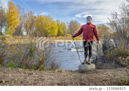 senior make hiker in his 70s with trekking poles on a shore of the Poudre River in Fort Collins, Colorado, fall scenery senior make hiker in his 70s with trekking poles on a shore of the Poudre River in Fort Collins, Colorado, fall scenery 133086925