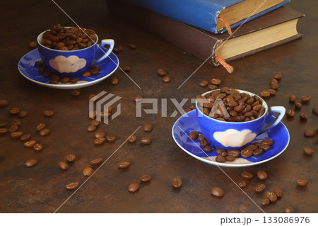 Coffee bean in the blue cups and vintage book stacking on wooden table in morning light Coffee bean in the blue cups and vintage book stacking on wooden table in morning light 133086976
