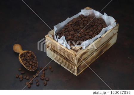 Closeup of roasted coffee beans in a small wooden crate, isolated on dark background. With wooden spoon. 133087855