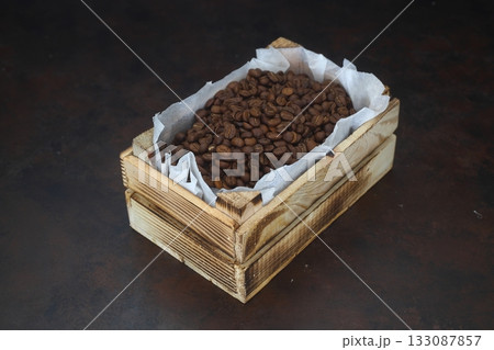 Closeup of roasted coffee beans in a small wooden crate, isolated on dark background. With wooden spoon. 133087857