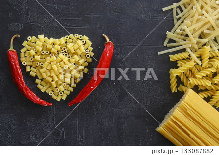 Pasta in the shape of a heart on a black background. With red hot chili peppers. 133087882