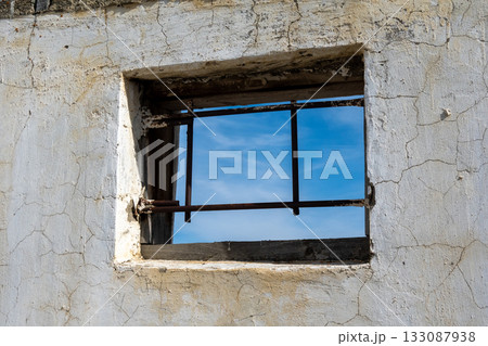 Rustic window frame revealing blue sky through its barred aperture 133087938