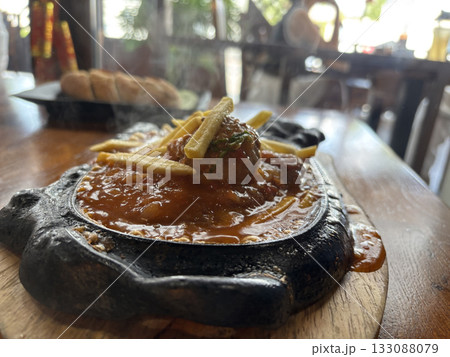 Sizzling Vietnamese Bo Ne with beef, a fried egg, and fries on a hot cast iron platter 133088079